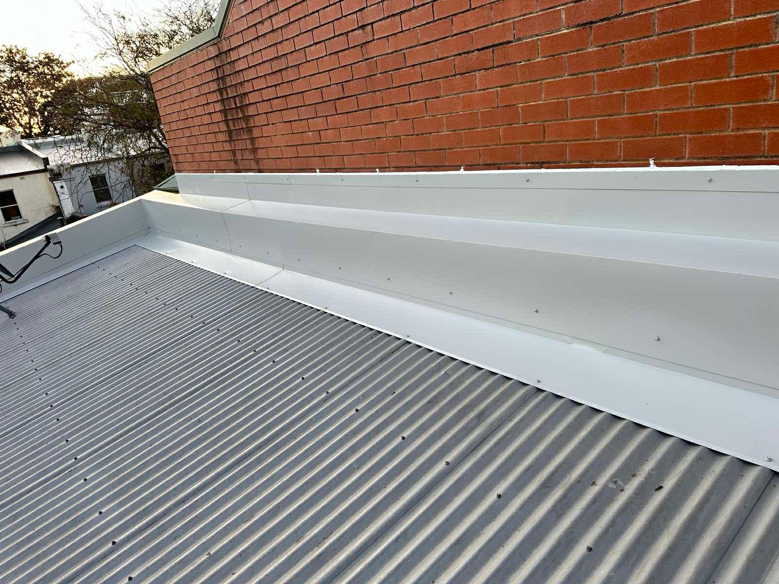 White corrugated roof with step flashing against brick wall